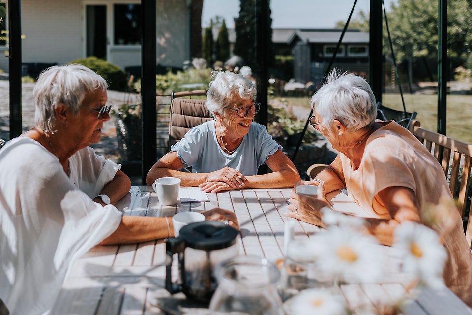 En grupp äldre utför en aktivitet. De sitter ner och fikar. På bordet står en blomma och ett tänt ljus.