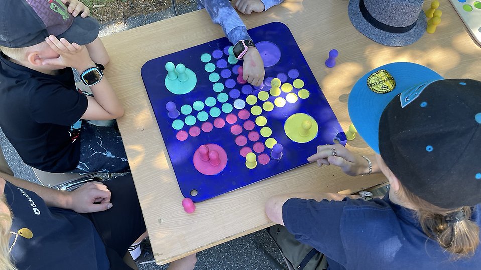 Lapset ja leirin vetäjä pelaavat peliä / Barn med sin ledare spelar ett brädspel