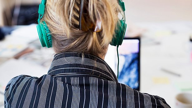 Person sitter framför dator, bärandes gröna hörlurar.