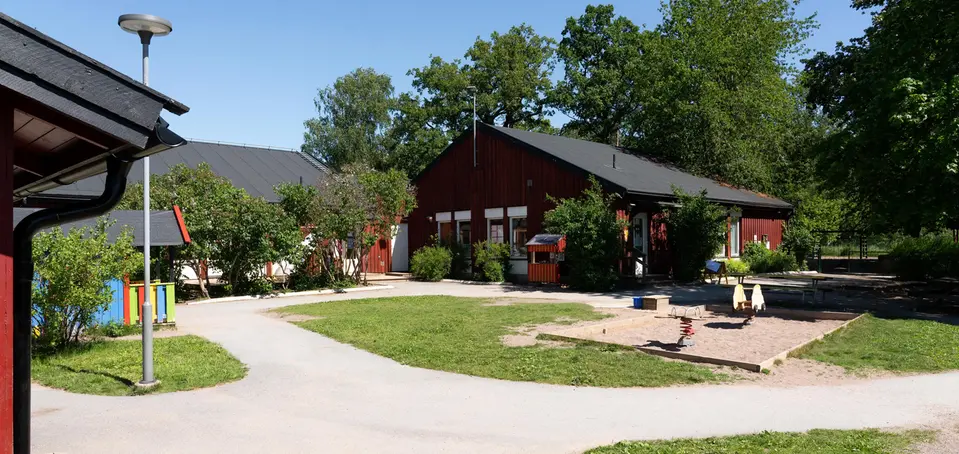 Bild på förskolan Bikupan, röda enplans hus som sitter ihop i grönskande miljö